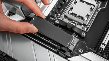 A person is installing an M.2 NVMe SSD into a modern motherboard socket, showcasing computer hardware assembly in progress.